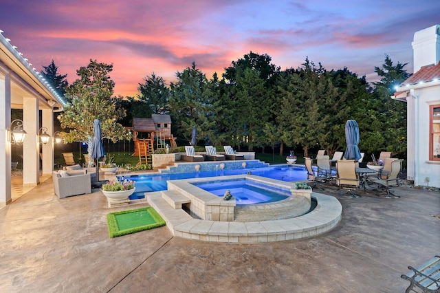 pool at dusk featuring an in ground hot tub, a playground, and a patio area