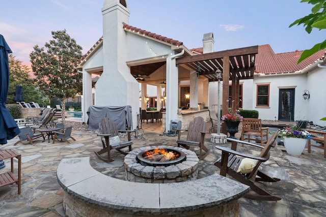 patio terrace at dusk with a pergola, a bar, and an outdoor fire pit