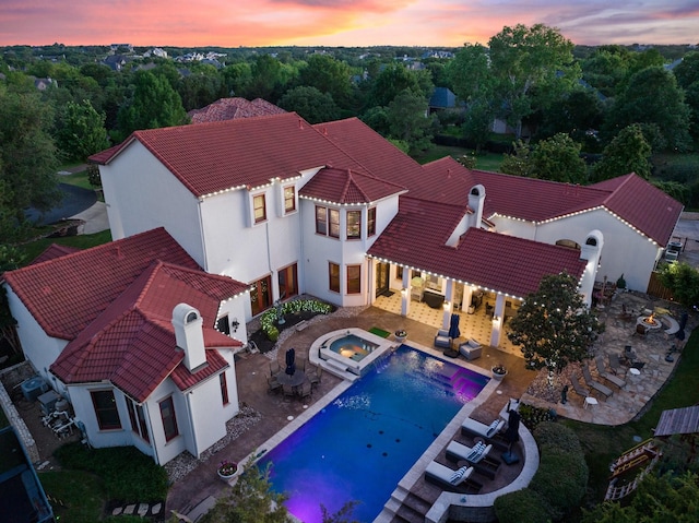 pool at dusk featuring an in ground hot tub and a patio