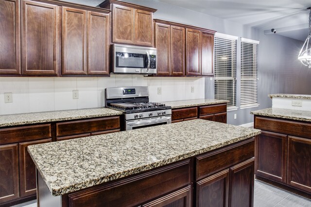 kitchen featuring stainless steel appliances, light stone countertops, a center island, pendant lighting, and decorative backsplash