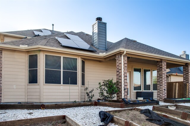 snow covered rear of property featuring central air condition unit and solar panels