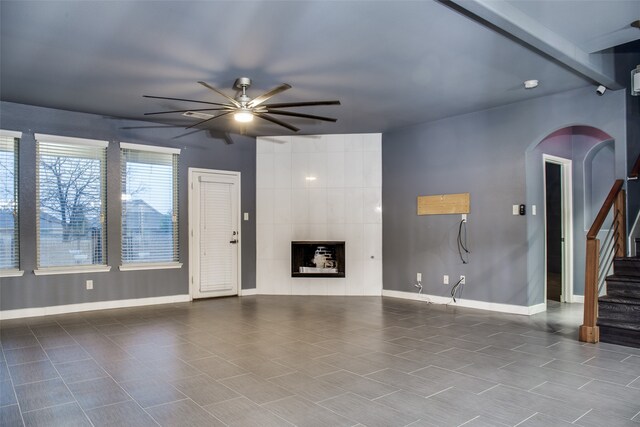 unfurnished living room with ceiling fan, beamed ceiling, and a tiled fireplace