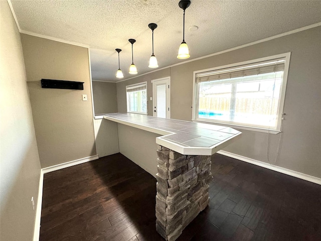 kitchen with kitchen peninsula, dark hardwood / wood-style floors, hanging light fixtures, crown molding, and a kitchen breakfast bar