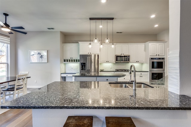 kitchen featuring sink, backsplash, dark stone countertops, white cabinets, and appliances with stainless steel finishes