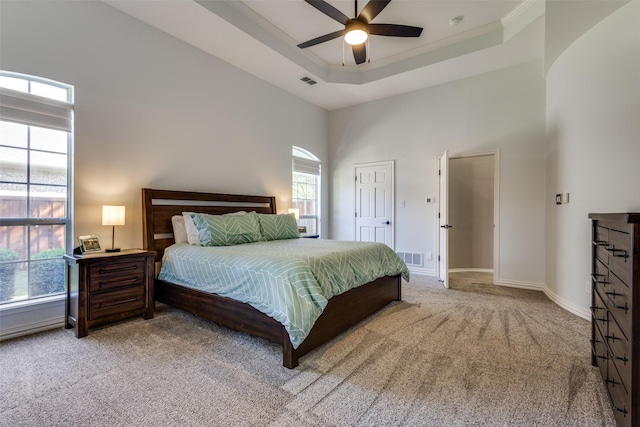 carpeted bedroom featuring a tray ceiling, ceiling fan, crown molding, and a towering ceiling