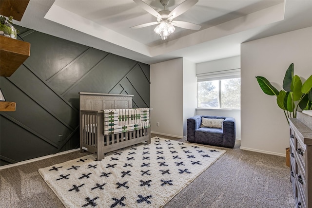 carpeted bedroom featuring a raised ceiling, ceiling fan, and a nursery area