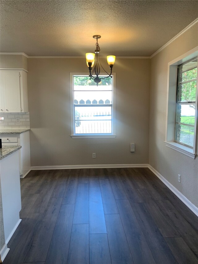 unfurnished dining area with dark wood-type flooring, a chandelier, a textured ceiling, and crown molding