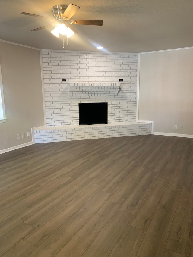 unfurnished living room featuring ceiling fan, dark hardwood / wood-style floors, a textured ceiling, crown molding, and a brick fireplace