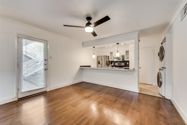 unfurnished living room featuring ornamental molding, hardwood / wood-style floors, ceiling fan, and stacked washer / dryer