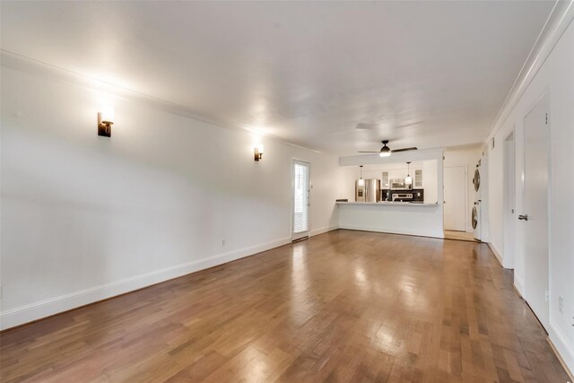 unfurnished living room featuring hardwood / wood-style floors, ceiling fan, stacked washer / drying machine, and ornamental molding