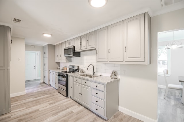 kitchen with light stone countertops, tasteful backsplash, stainless steel appliances, sink, and light hardwood / wood-style floors