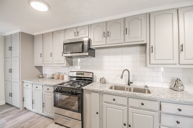 kitchen featuring light stone countertops, sink, tasteful backsplash, light hardwood / wood-style flooring, and appliances with stainless steel finishes