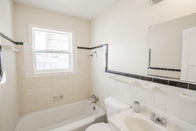 full bathroom featuring vanity, tiled shower / bath combo, tile walls, and toilet