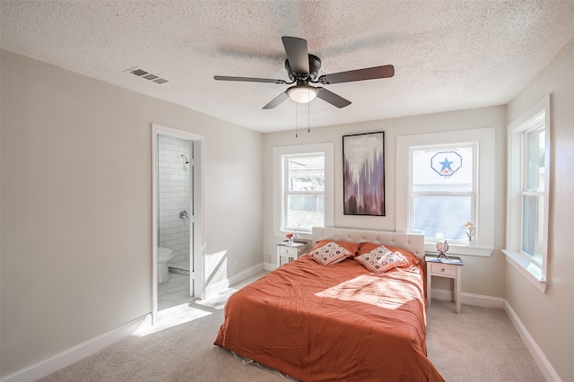 bedroom featuring ceiling fan, ensuite bathroom, a textured ceiling, and light carpet