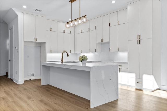 kitchen featuring white cabinetry, sink, hanging light fixtures, light hardwood / wood-style floors, and a kitchen island with sink