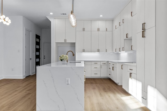 kitchen featuring white cabinetry, sink, decorative light fixtures, and light wood-type flooring