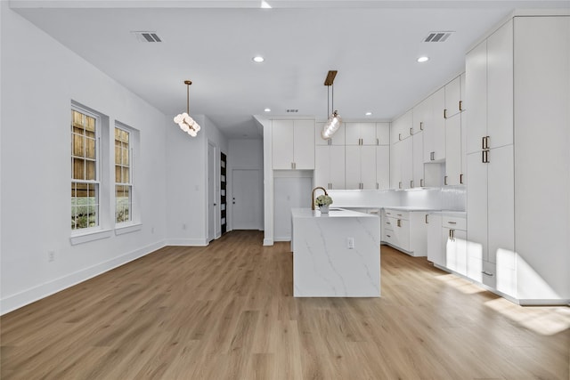 kitchen featuring a center island with sink, white cabinets, hanging light fixtures, and light wood-type flooring