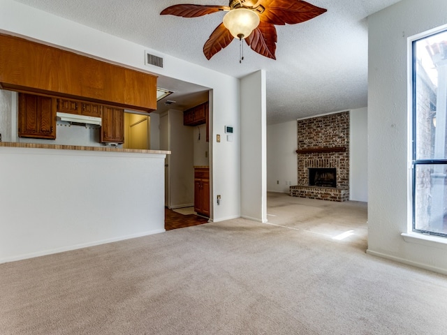 unfurnished living room with a textured ceiling, a fireplace, light colored carpet, and ceiling fan