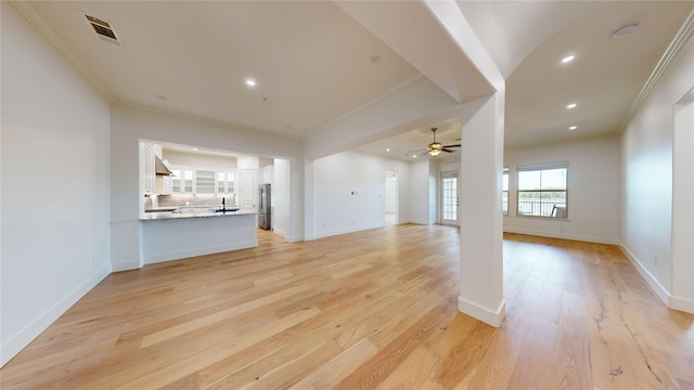 unfurnished living room featuring ceiling fan, ornamental molding, sink, and light wood-type flooring