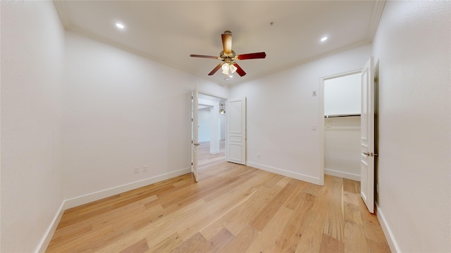 unfurnished bedroom featuring ornamental molding, a walk in closet, ceiling fan, and light wood-type flooring