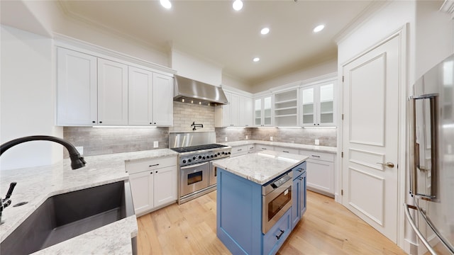 kitchen with high end appliances, light stone counters, white cabinetry, and wall chimney exhaust hood