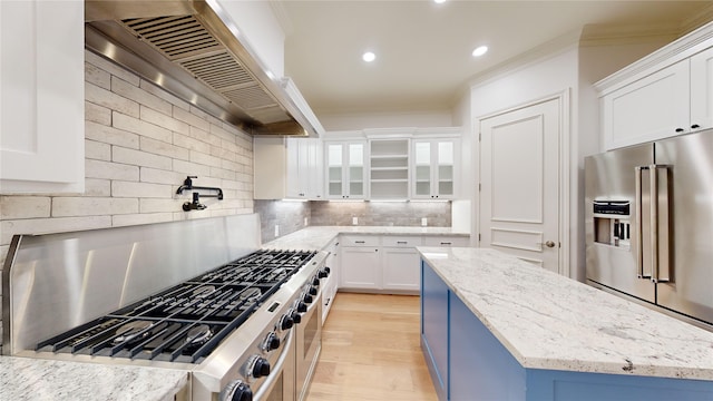 kitchen featuring tasteful backsplash, stainless steel appliances, a kitchen island, white cabinetry, and wall chimney range hood