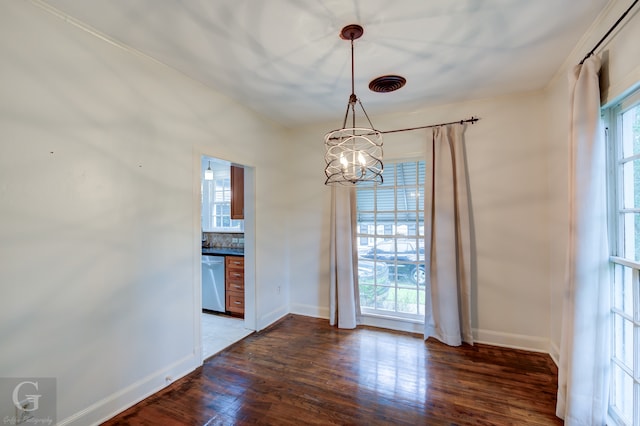 unfurnished dining area with dark wood-type flooring, crown molding, and a notable chandelier