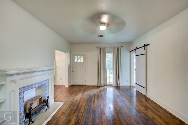 unfurnished living room featuring a barn door, ceiling fan, dark wood-type flooring, and ornamental molding