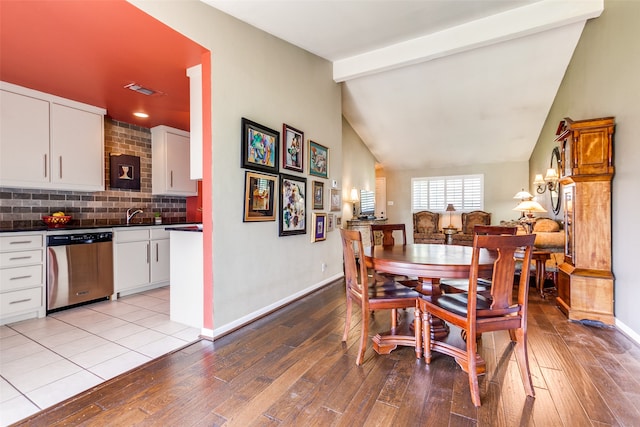 dining space featuring light wood-type flooring and vaulted ceiling with beams