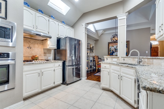 kitchen featuring appliances with stainless steel finishes, light stone counters, vaulted ceiling with skylight, sink, and white cabinetry