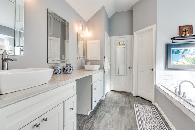 bathroom featuring hardwood / wood-style flooring, vanity, a relaxing tiled tub, and lofted ceiling