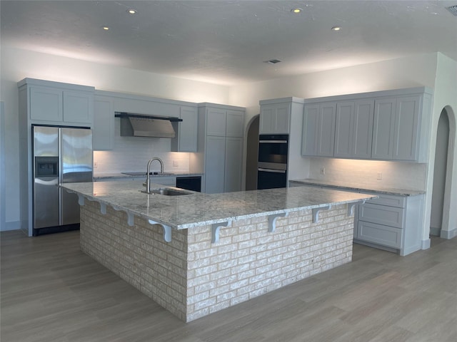 kitchen with light stone counters, wall chimney range hood, tasteful backsplash, and black appliances