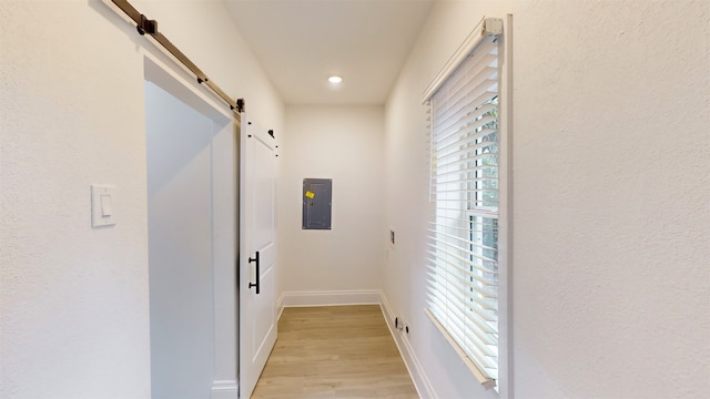 corridor with electric panel, a barn door, and light hardwood / wood-style floors