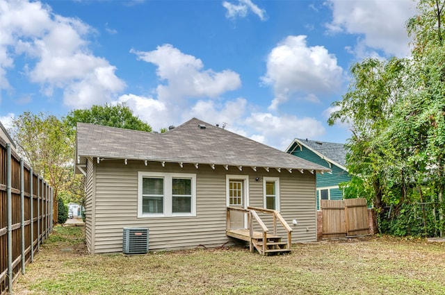 rear view of property featuring central air condition unit and a lawn