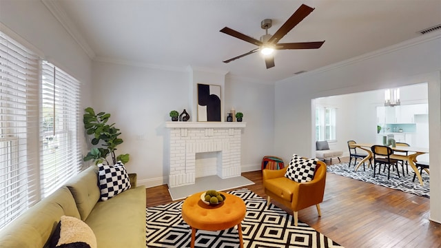 living room with a brick fireplace, hardwood / wood-style flooring, crown molding, and ceiling fan