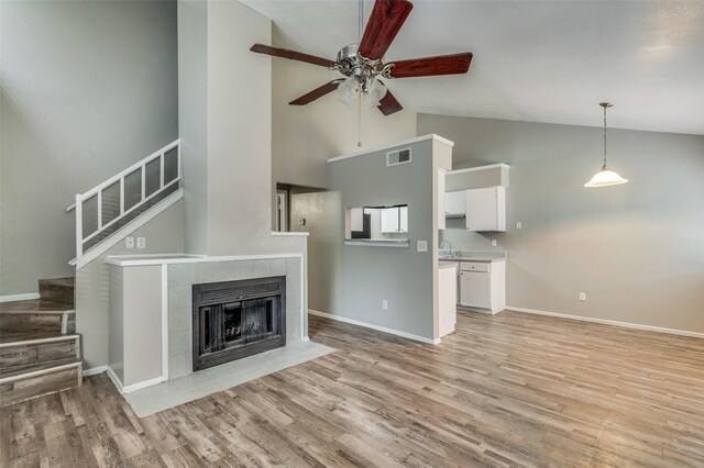 unfurnished living room featuring light hardwood / wood-style floors, a tiled fireplace, and high vaulted ceiling