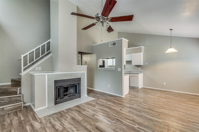 unfurnished living room with sink, ceiling fan, high vaulted ceiling, light hardwood / wood-style floors, and a tiled fireplace