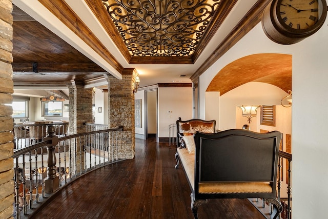 hallway featuring crown molding, a tray ceiling, dark hardwood / wood-style flooring, and decorative columns