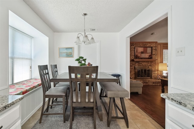 dining room featuring a notable chandelier, a fireplace, light wood-type flooring, and a textured ceiling