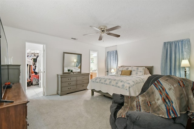 bedroom featuring light carpet, a textured ceiling, ceiling fan, a spacious closet, and a closet