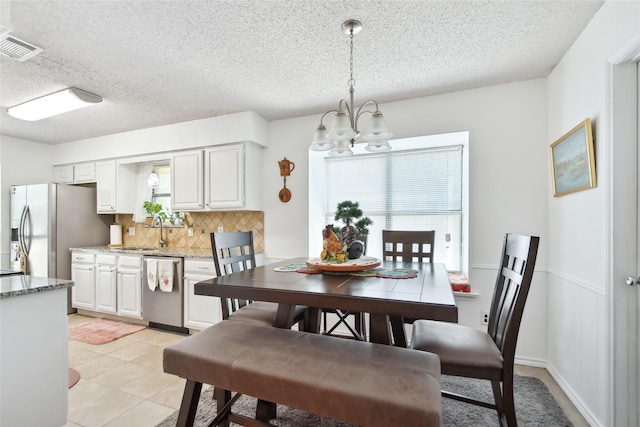 dining space featuring sink, light tile patterned floors, a textured ceiling, and a notable chandelier