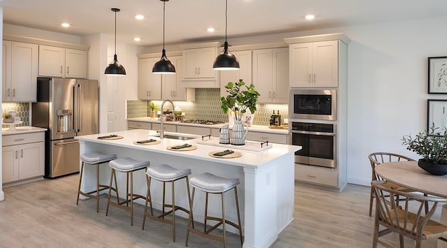 kitchen featuring appliances with stainless steel finishes, decorative light fixtures, sink, an island with sink, and light hardwood / wood-style floors