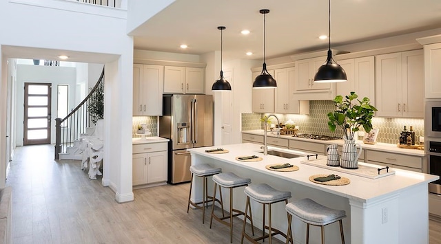 kitchen featuring stainless steel appliances, white cabinetry, an island with sink, and decorative light fixtures