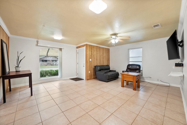 sitting room with wood walls, ceiling fan, light tile patterned floors, and ornamental molding