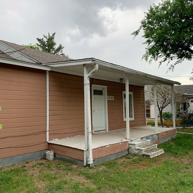 view of exterior entry featuring a lawn and a porch