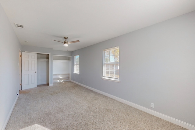 unfurnished bedroom with ceiling fan, multiple closets, and light colored carpet