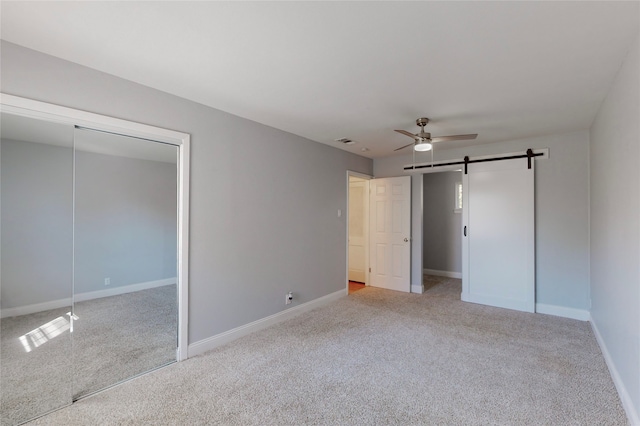 unfurnished bedroom with a barn door, ceiling fan, a closet, and light colored carpet