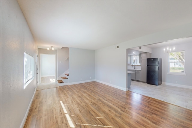 unfurnished living room featuring sink, an inviting chandelier, and light hardwood / wood-style flooring