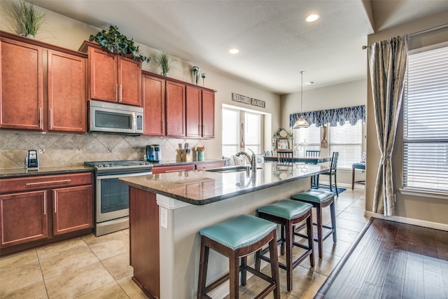 kitchen with light hardwood / wood-style floors, hanging light fixtures, a kitchen island with sink, a kitchen breakfast bar, and appliances with stainless steel finishes