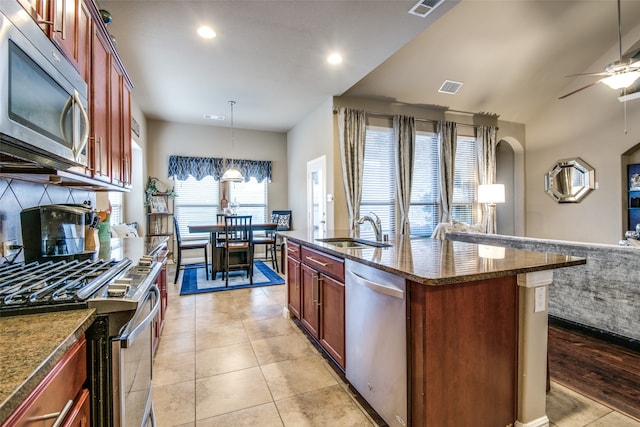 kitchen featuring a center island with sink, sink, ceiling fan, pendant lighting, and appliances with stainless steel finishes